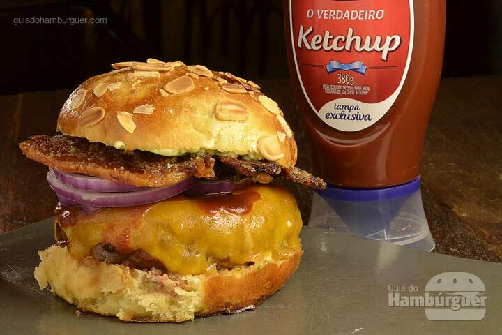 Wild Bite Burger: Pão com amêndoas, hambúrguer de 180g grelhado no carvão, queijo cheddar, cebola roxa, smoked bacon, barbecue de tabaco de corda e molho béarnaise de Wild Turkey Bourbon. -  R$ 29  - SP Burger Fest