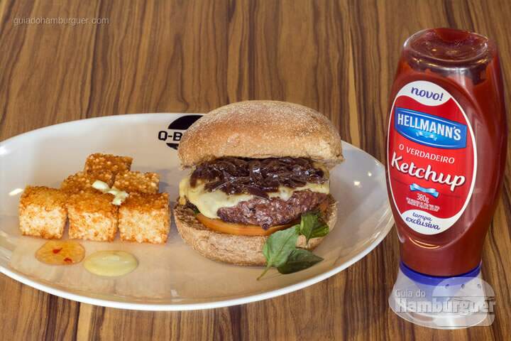 Q-Burger Onion: Hambúrguer bovino no pão australiano, queijo muçarela, manjericão e tomate caqui com chutney de cebolas levemente adocicado. Acompanha dadinhos de tapioca com geleia de pimenta. -  R$35,90 