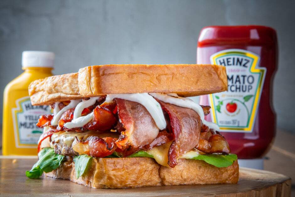 Pão Quadrado, hambúrguer bovino de 110g, 150g de bacon artesanal fatiado, queijo estepe, rúcula e maionese 2 alhos (alho poró e alho roxo)