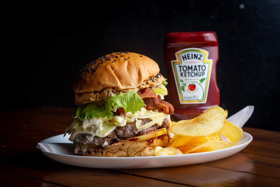 Pão branco com gergelim, 160g de hambúrguer preparado com picanha, bacon crocante, ovo frito na manteiga, mussarela, parmesão, catupiry, alface americana, tomate, molho barbecue e maionese de cebola caramelizada e alho